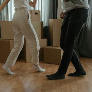 Two people dance joyfully amidst moving boxes in their new home.